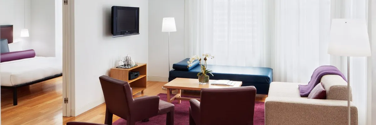 A wide view of a hotel suite with a living area and bedroom doorway.