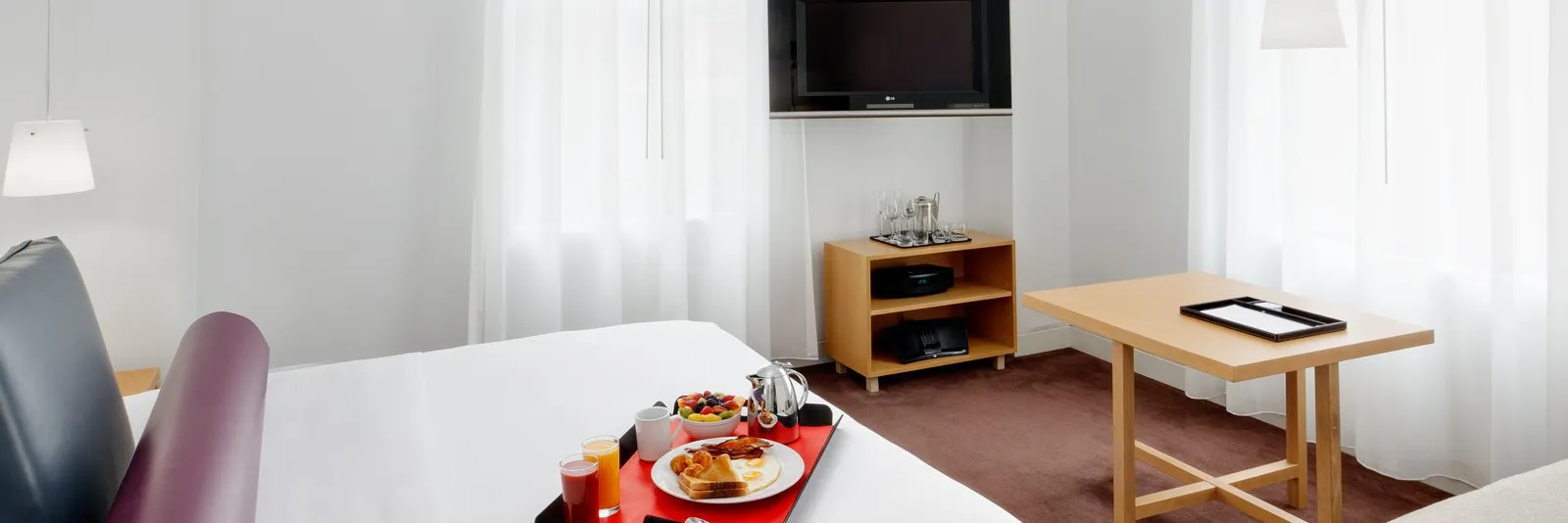 A hotel room with a bed, a table, a TV, and a breakfast tray.